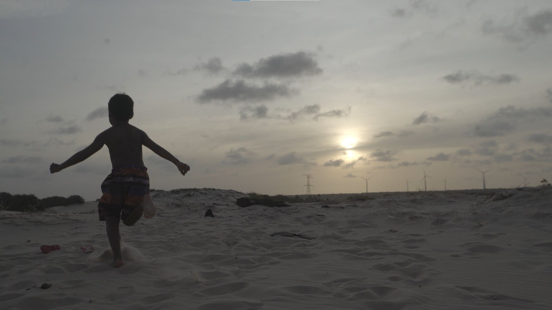 No canto esquerdo da imagem, vemos um garoto correr em uma praia.
