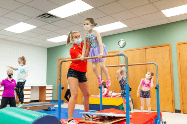 gymnastics instructor helping a young girl on the uneven bar during a gymnastics class