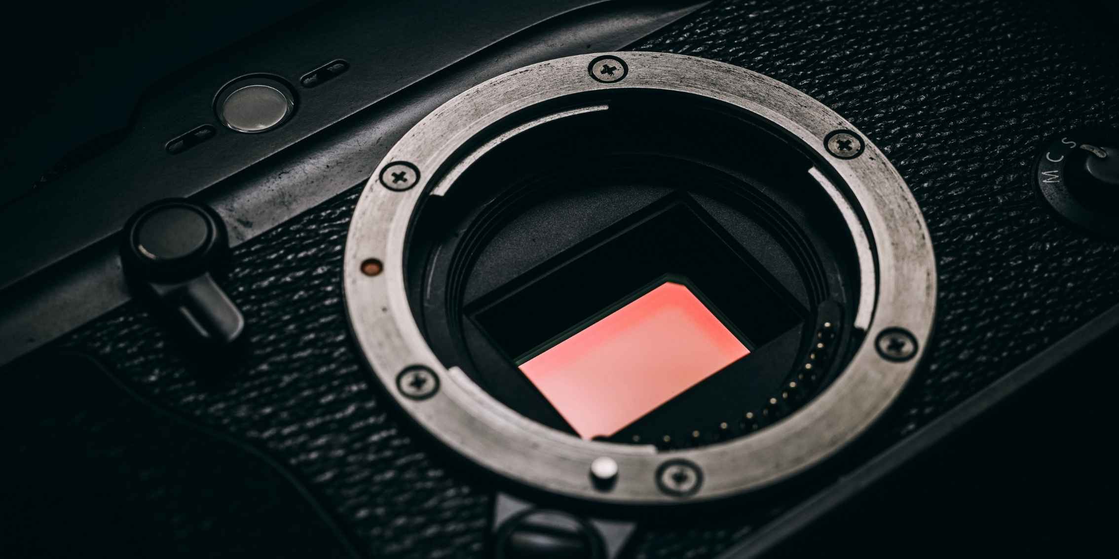 Close-up of a camera sensor with a reddish hue, surrounded by a metal ring and screws.