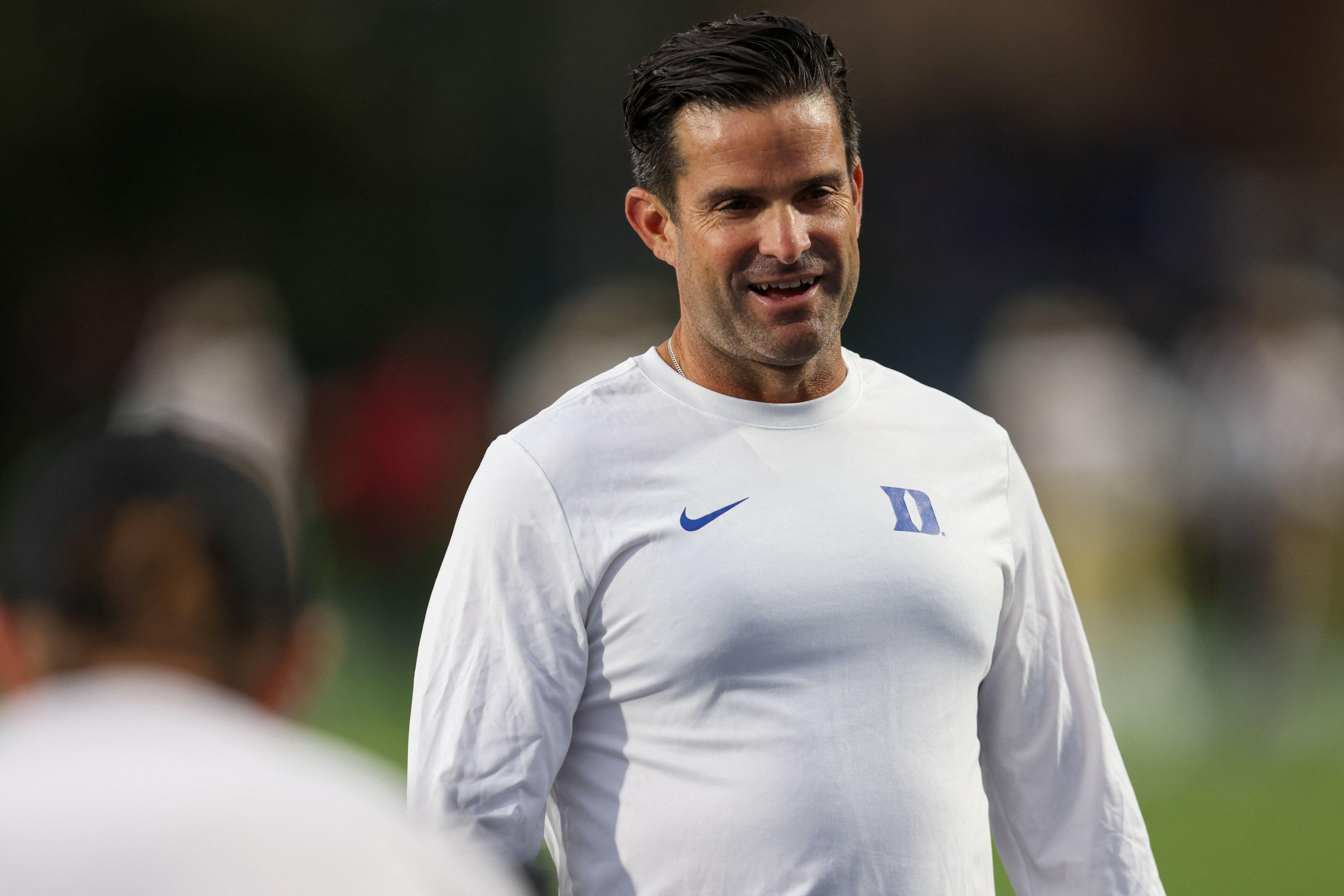 Duke football coach smiling on the sideline in a white Duke shirt Duke football coach smiling on the sideline in a white Duke shirt