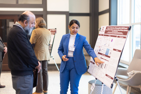 A student points at a research poster board while a judge looks at it.