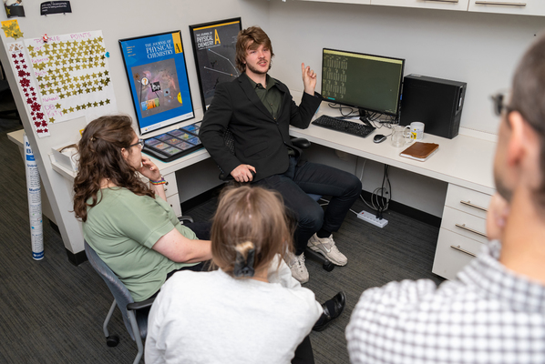 Three students and a professor talk in a science lab.
