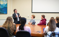 A professor speaks to students sitting around a large table during a seminar class.