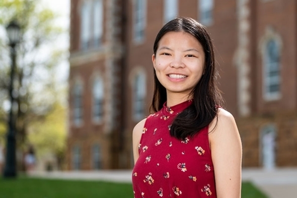 Nicole McKellar smiles in front of Old Main on the University of Arkansas campus. She is wearing a red floral sleeveless top.