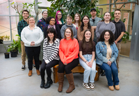 A group of creative writing students and their professor gather for a photo in a campus greenhouse.
