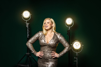 A woman wearing a long sleeve shiny dress, posing in front of spotlights. 