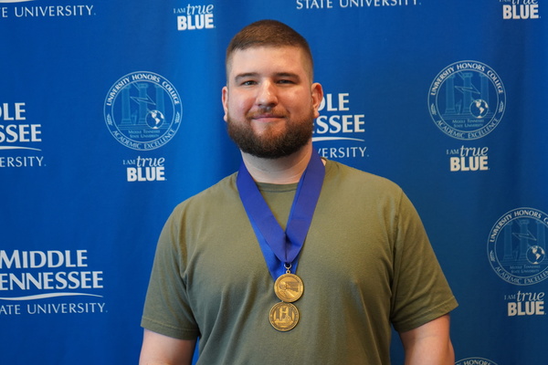 Student wearing two medals smiles in front of backdrop