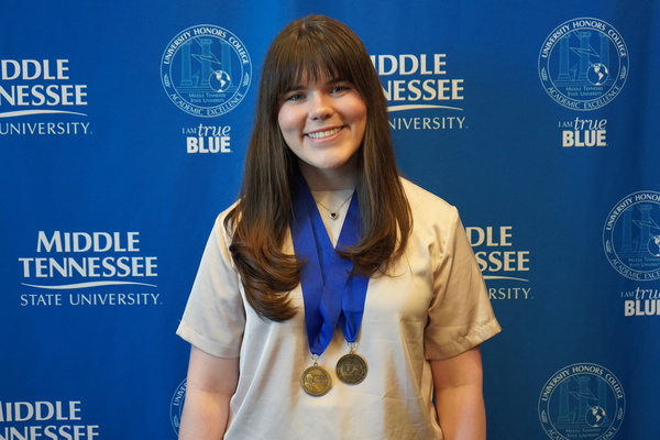 woman with long, dark hair and wearing two medals stands in front of backdrop