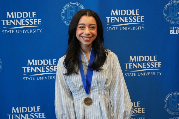 MTSU studnets smiles and wears medal, standing in front of backdrop