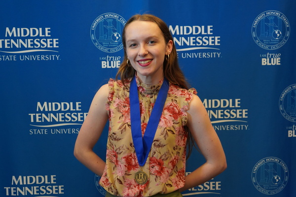 MTSU student wearing Honors thesis defense medal stands in front of backdrop smiling