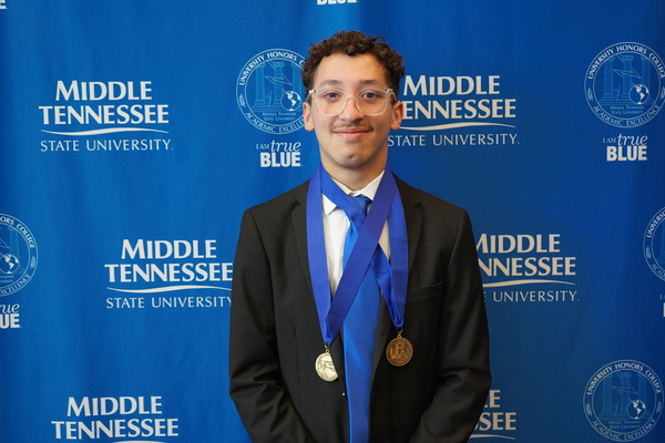 Smiling MTSU student just successfully defended Honors thesis, wearing medals in front of backdrop
