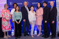 Eight people pose in front of a blue backdrop with the College logo