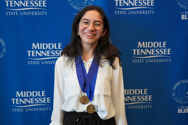 Smiling MTSU student just successfully defended Honors thesis, wearing medals in front of backdrop