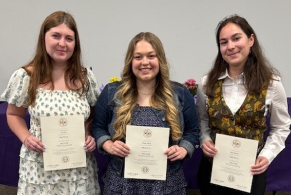 Three students hold certificates after being inducted into the education honor society