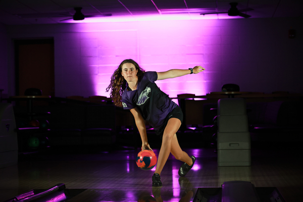 A person throwing a bowling ball with a purple glow behind them.
