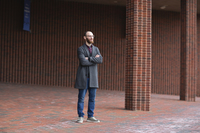 SUNY Potsdam alumnus Brandon Rodriguez stands in front of a brick college building.