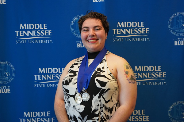 Smiling MTSU student just successfully defended Honors thesis, wearing medals in front of backdrop