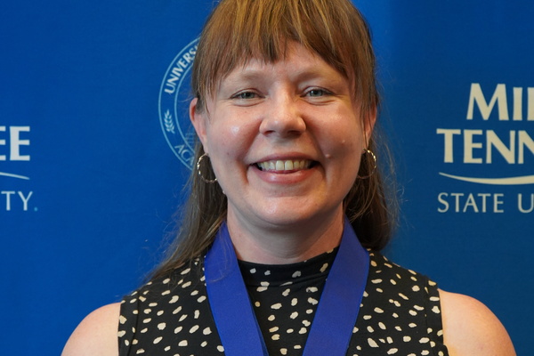 Smiling MTSU student just successfully defended Honors thesis, wearing medals in front of backdrop