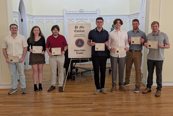 Seven students stand on a stage holding certificates after their honor society induction.