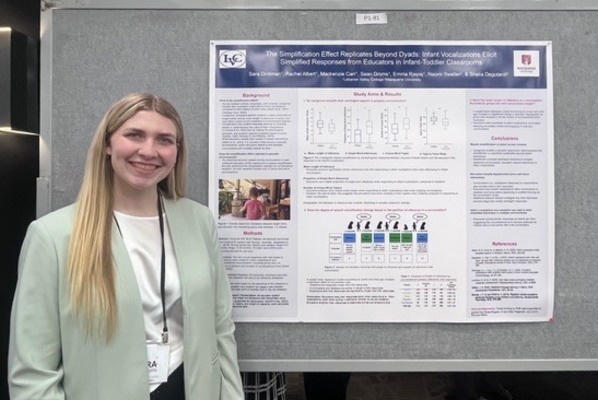 A student stands alongside a research poster at a conference
