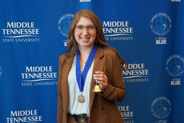Smiling MTSU student just successfully defended Honors thesis, wearing medal in front of backdrop