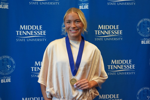 Smiling MTSU student just successfully defended Honors thesis, wearing medal in front of backdrop