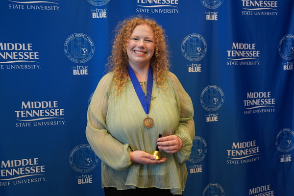 Smiling MTSU student just successfully defended Honors thesis, wearing medal in front of backdrop