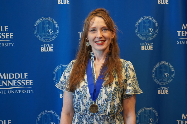Smiling MTSU student just successfully defended Honors thesis, wearing medal in front of backdrop
