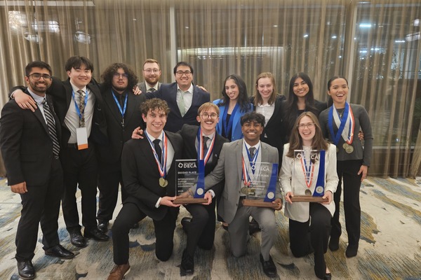 Kettering University students, dressed in business attire, pose together at an indoor conference, several holding award plaques and medals.