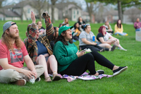 Students sitting in the grass cheer while listening to concert performances at SUNY Potsdam's Marshall Park bandshell.