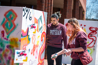 Students in SUNY Potsdam sweatshirts paint large panels with spraypaint during a festival.