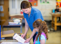 A professor holds out a coloring sheet for a girl in a school program.