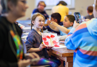 A girl smiles as she holds up a painted picture of tulips during a field trip.