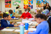 Children paint in a studio, with art on the walls in the background.