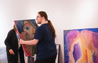 A student intern carries oil paintings while helping to set up an art exhibition.