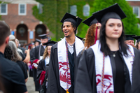Graduates wearing mortarboards and SUNY Potsdam Bears stoles process through the Academic Quad at SUNY Potsdam.