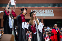 A group of graduates smile and pose for the camera while holding their diplomas at SUNY Potsdam's Commencement.