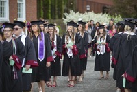 A line of graduates wearing their mortarboards and gowns, along with colorful stoles and cords, wait to cross the stage.