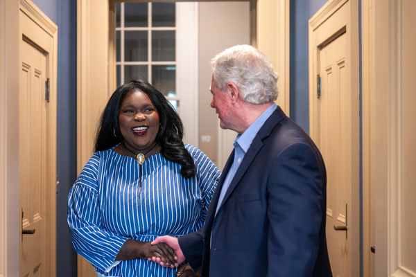 A student and university administrator shake hands in a hallway.