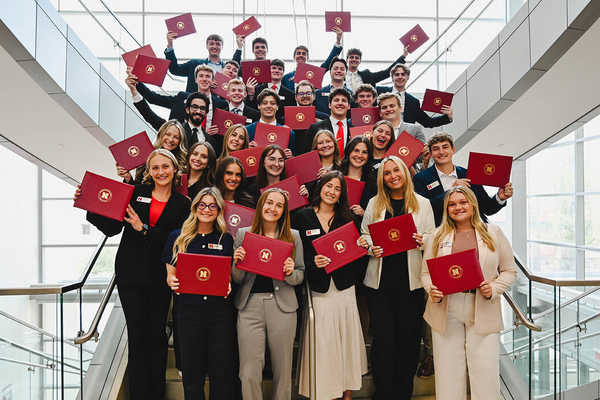 About 30 Husker students pose on a staircase in Howard L. Hawks Hall, holding certificates.
