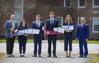 Students in business attire holding awards pose for photos next to faculty members in the Quad.