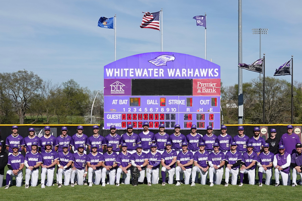 A group of college baseball players posing in front of a large scoreboard.