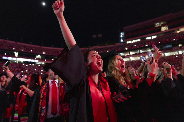 students in caps and gowns cheer in stadium to celebrate graduation