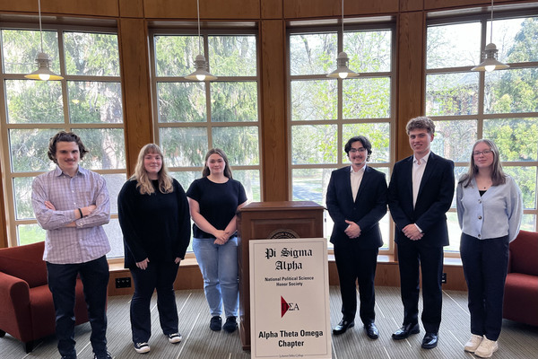 Six students stand around a lectern with a sign for Pi Sigma Alpha.