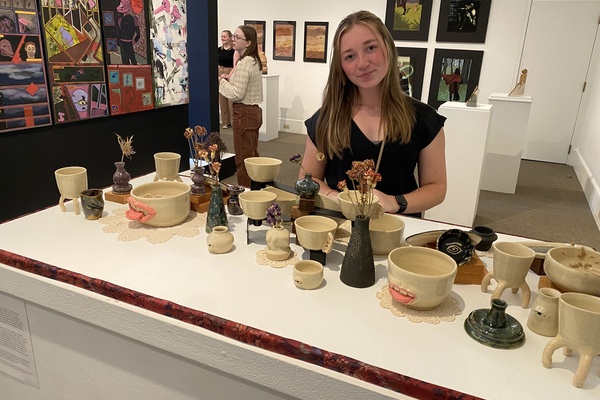 A student stands in the art gallery behind a table featuring her pottery bowls.