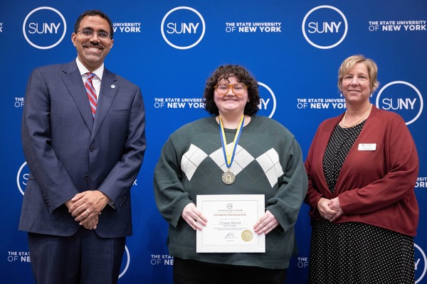 Chancellor King, Chase Bond and President Smith pose in front of a SUNY backdrop.