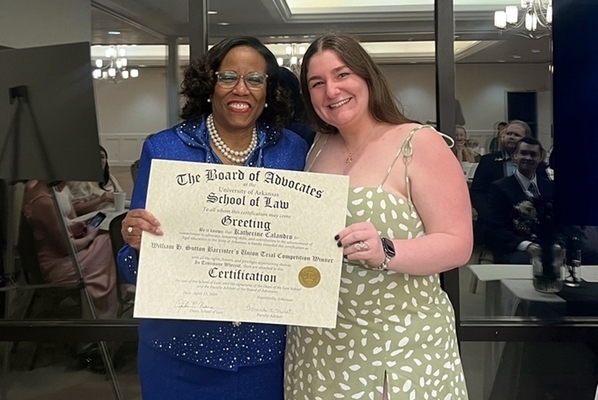 Katherine Calandro, wearing green dress, receiving a certificate from Dean Cynthia Nance, wearing blue dress, at the end-of-year banquet. 
