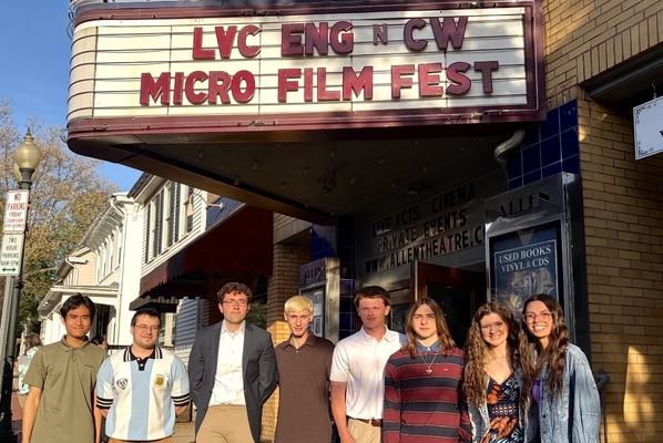 Eight students stand on the sidewalk with a marquee above them highlighting the Micro Film Fest.