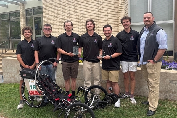Six team members and an advisor stand in front of brick building holding two trophies with their e-Human Powered Vehicle on display in front of them.