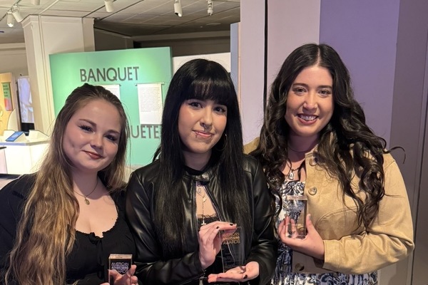Three female students hold trophies.